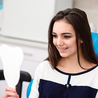 Girl smiling while looking at braces in mirror