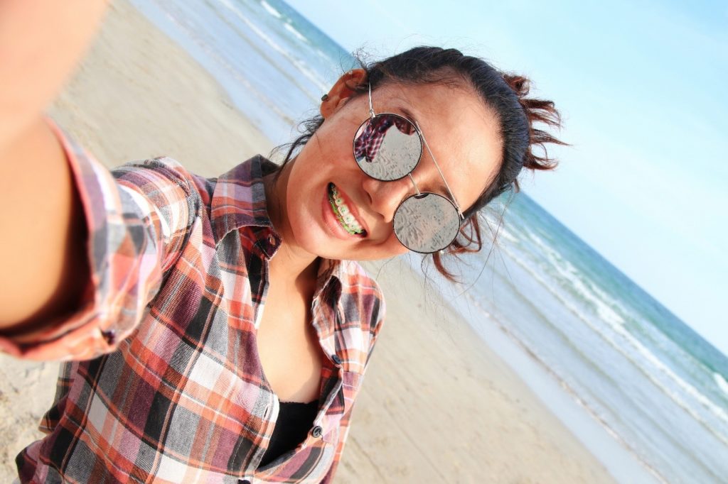 Woman with braces smiling while taking a selfie at the beach