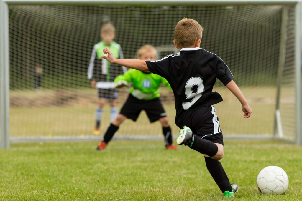 Child kicking soccer ball into the net