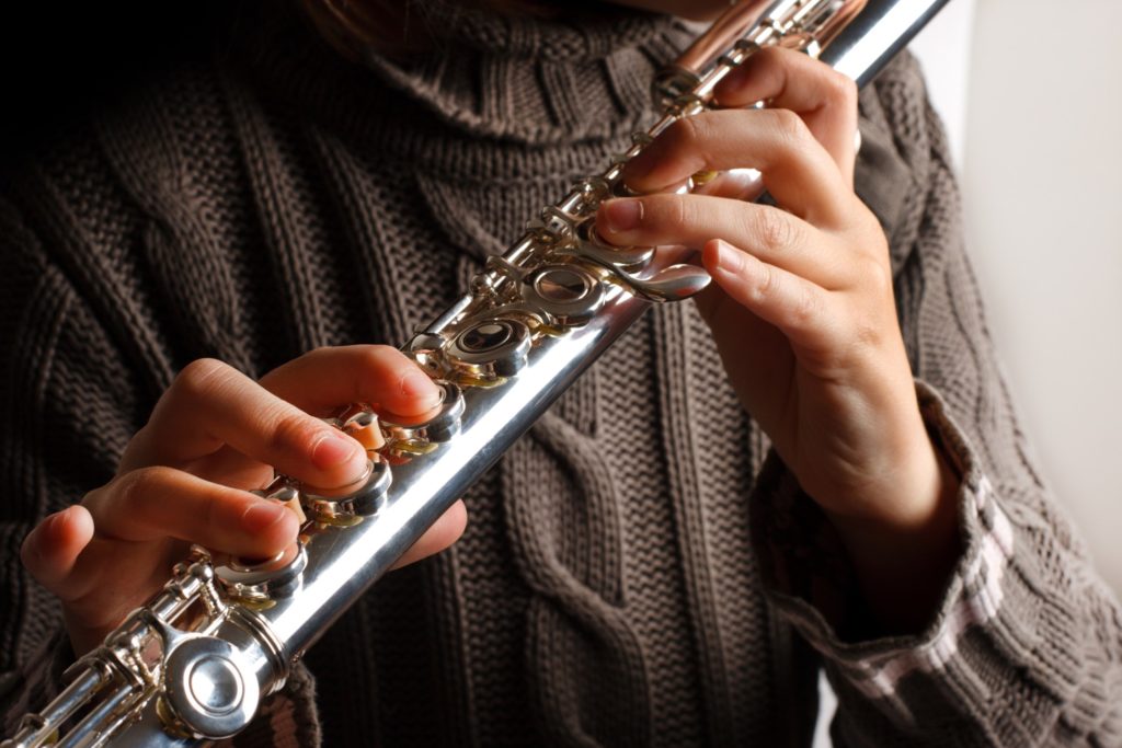 Closeup of woman in brown sweater playing the flute