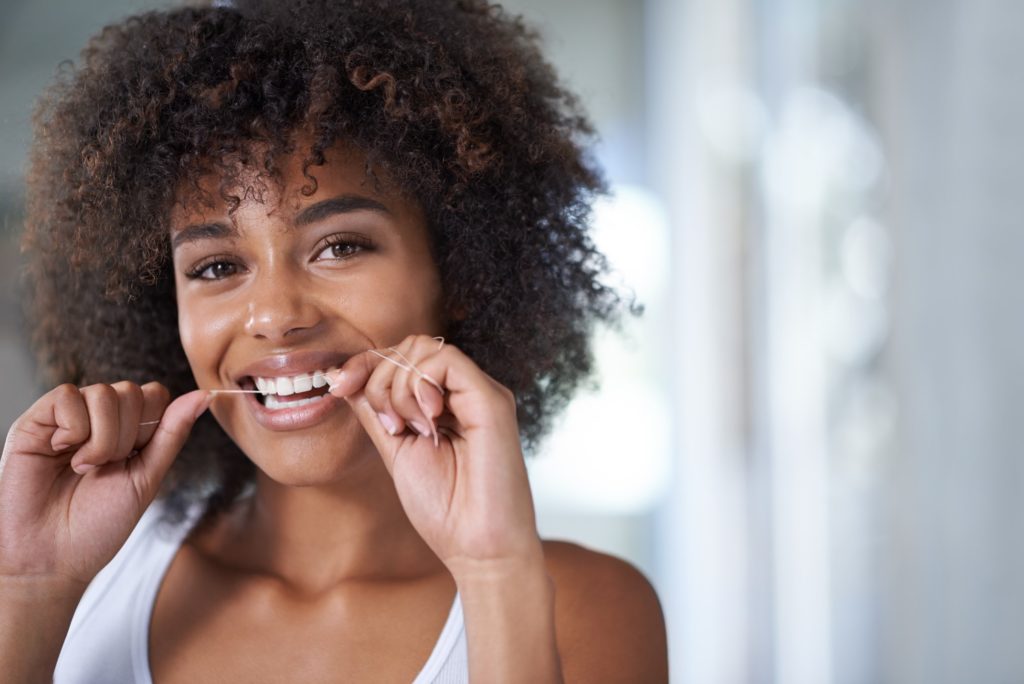 Closeup of woman smiling while flossing her teeth